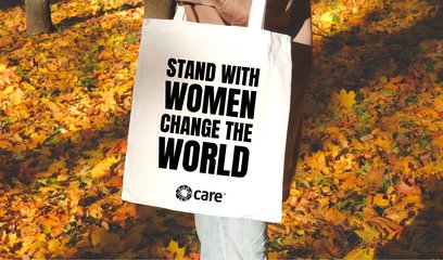 Woman holding a tote bag in the autumn leaves with 'stand with women change the world' on it