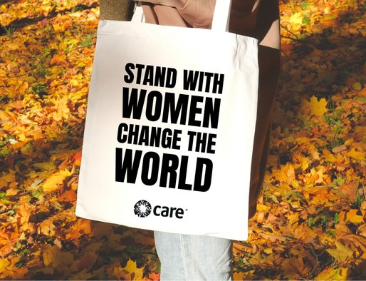 Woman holding a tote bag in the autumn leaves with 'stand with women change the world' on it